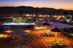 Yakout Merzouga Luxury Camp illuminated luxury tents and pool area at dusk with desert dunes backdrop and outdoor seating