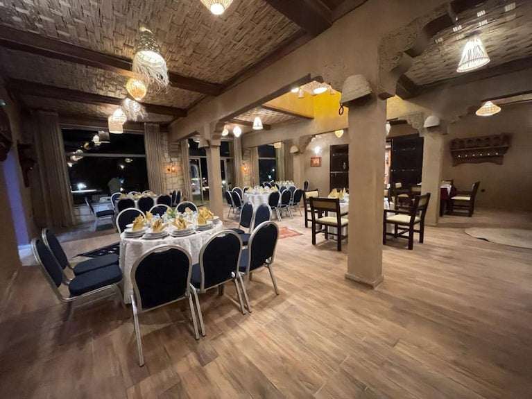 Dining area at Yakout Merzouga Luxury Camp featuring round tables set with white linens, navy blue chairs, and warm ambient lighting