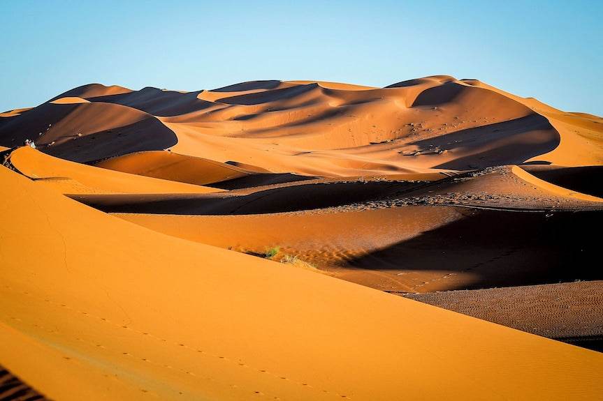 Golden sand dunes with smooth curves and shadows in the Moroccan desert representing Yakout Merzouga Luxury Camp surroundings