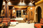 Yakout Merzouga Luxury Camp indoor lounge area featuring warm yellow walls, traditional Moroccan patterned cushions, wooden pillars, and tribal decor