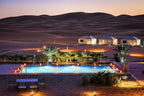 Yakout Merzouga Luxury Camp with illuminated white luxury tents near a glowing pool surrounded by desert dunes at sunset