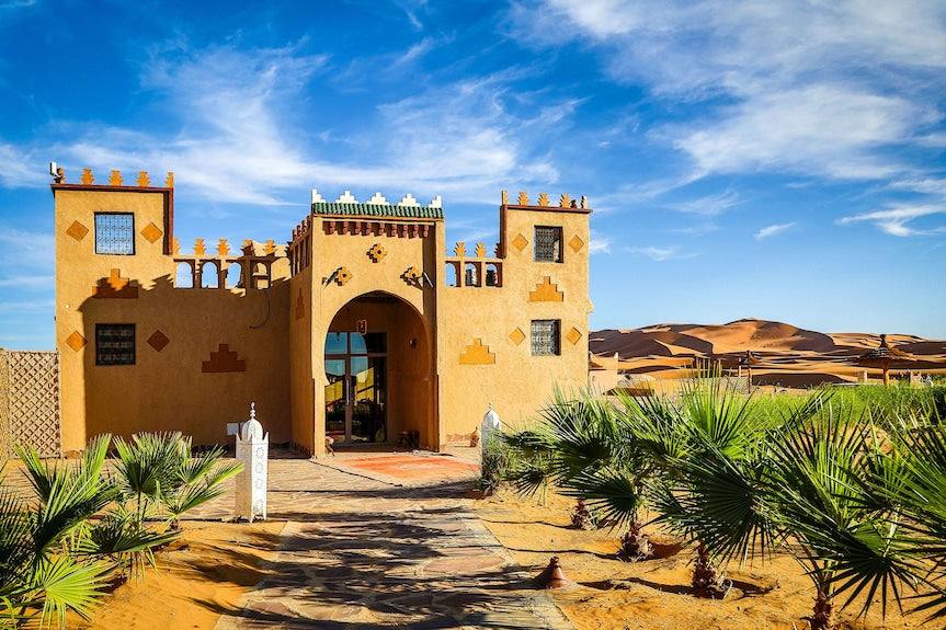 Yakout Merzouga Luxury Camp desert accommodation with traditional ochre and green Moroccan architecture under blue sky