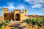 Yakout Merzouga Luxury Camp desert accommodation with traditional ochre and green Moroccan architecture under blue sky