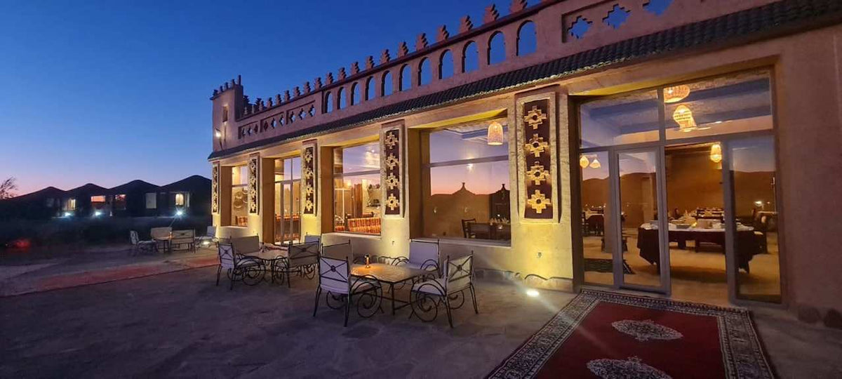 Yakout Merzouga Luxury Camp exterior at twilight featuring traditional Moroccan architectural details and outdoor seating area