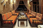 Yakout Merzouga Luxury Camp sitting area with traditional patterned orange cushions on dark wooden benches and a table with Moroccan snacks