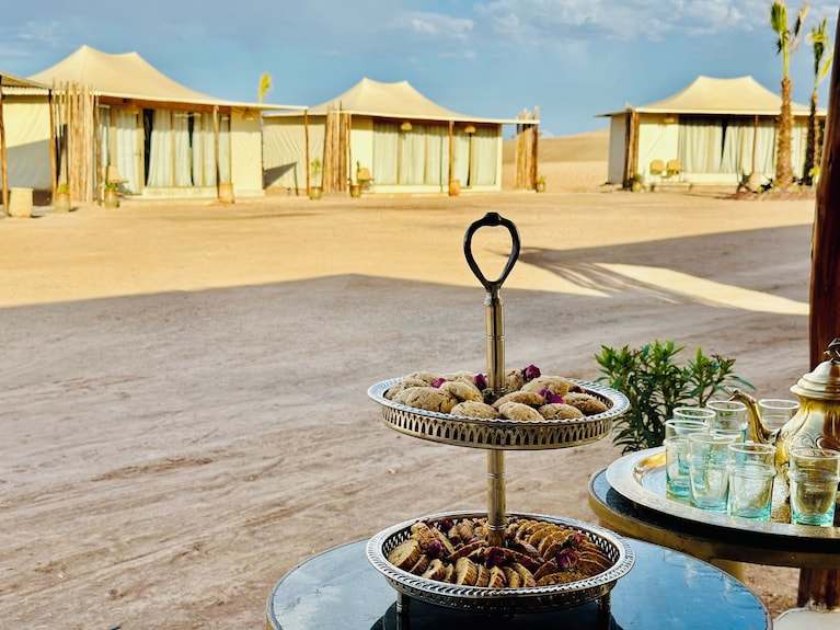Yes We Camps Luxury Lodge & Spa featuring beige luxury tents in desert with trays of Moroccan pastries and glassware in foreground