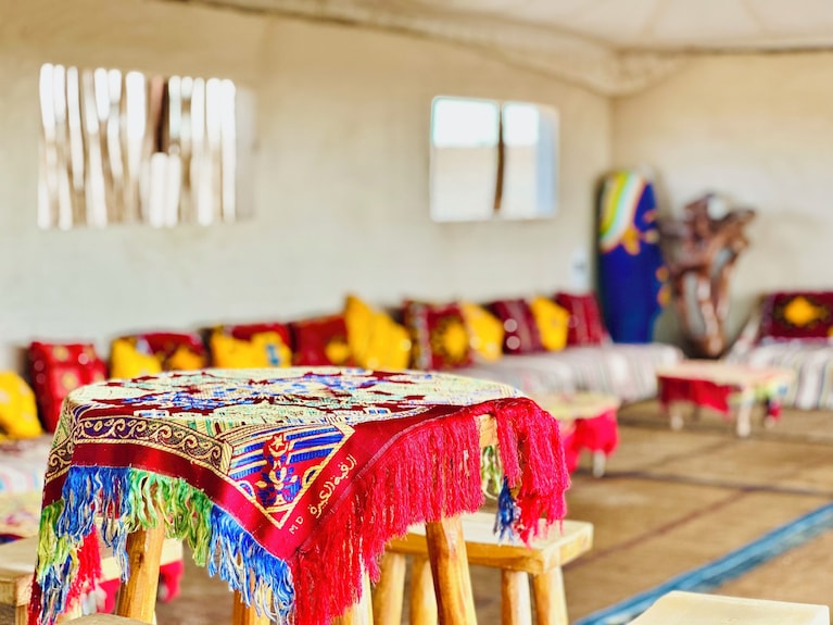 Yes We Camps Luxury Lodge & Spa interior with colorful patterned tablecloth on wooden table, vibrant cushions on beige seating