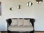Dark carved wooden sofa with beige cushions and circular seat cushion near white wall with gold-framed eye-shaped mirrors