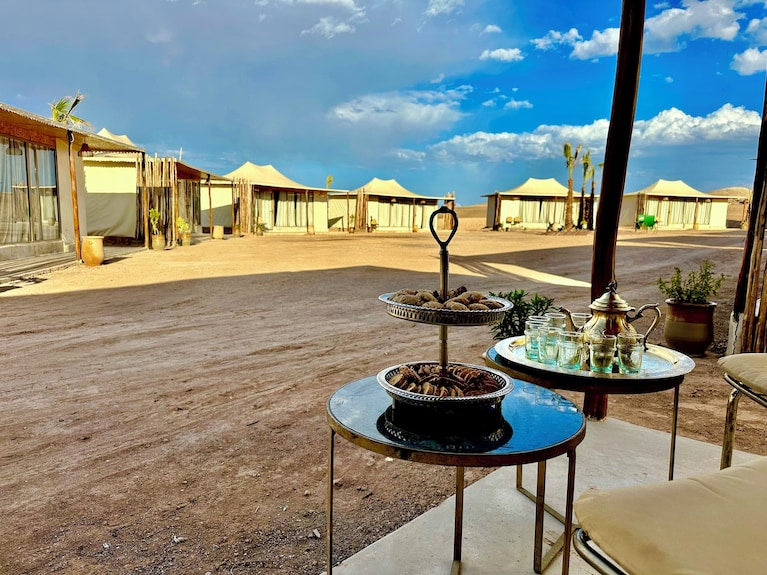 Yes We Camps Luxury Lodge & Spa outdoor desert lounge area with beige tents, metal tables with Moroccan tea set and pastries