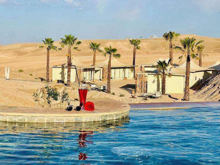 Yes We Camps Luxury Lodge & Spa desert retreat with beige tents, palm trees, and a clear blue pool with a red drink on the edge