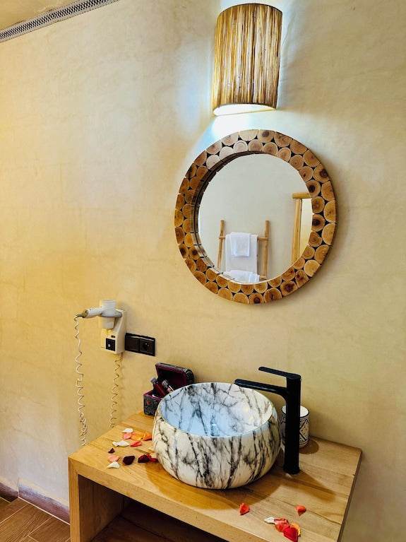 Bathroom vanity with a marble vessel sink, black faucet, wooden countertop, round wooden frame mirror, and wall lamp, featuring Yes We Camps Luxury Lodge & Spa style