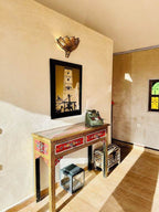Wooden console table with colorful red floral drawers under Moroccan-style wall lamp and framed tower art in beige walled room at Yes We Camps Luxury Lodge & Spa