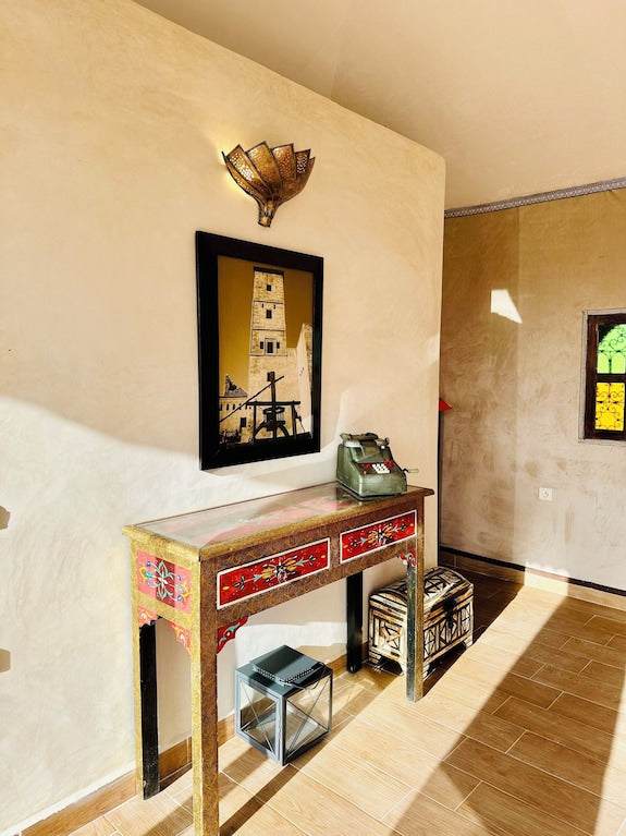 Wooden console table with colorful red floral drawers under Moroccan-style wall lamp and framed tower art in beige walled room at Yes We Camps Luxury Lodge & Spa