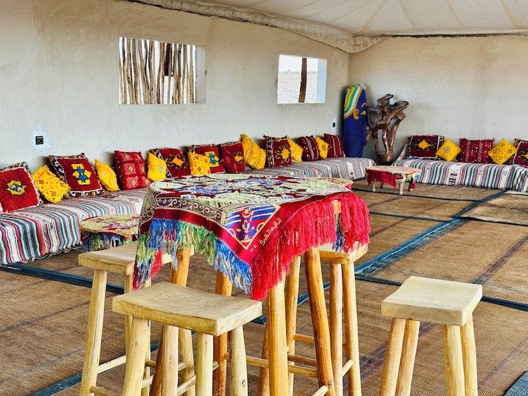 Yes We Camps Luxury Lodge & Spa interior with traditional Moroccan seating, colorful cushions, wooden stools, and fringed patterned tablecloth