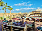 Yes We Camps Luxury Lodge & Spa outdoor seating area with wooden furniture, pool, umbrellas, and desert landscape under blue sky