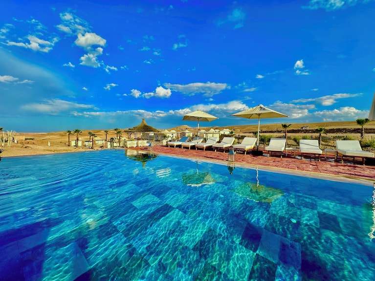 Outdoor swimming pool with clear blue water and sun loungers under umbrellas at Yes We Camps Luxury Lodge & Spa desert resort