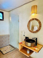 Yes We Camps Luxury Lodge & Spa bathroom with rustic wooden countertop, decorative round mirror, black sink and glass shower partition