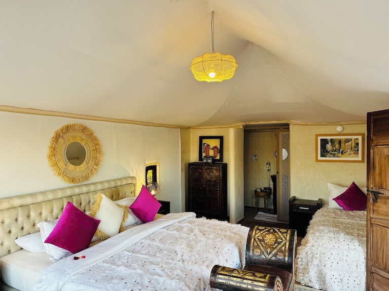 Yes We Camps Luxury Lodge & Spa tent interior featuring two beds with white and purple bedding, wooden chest, and rustic decor